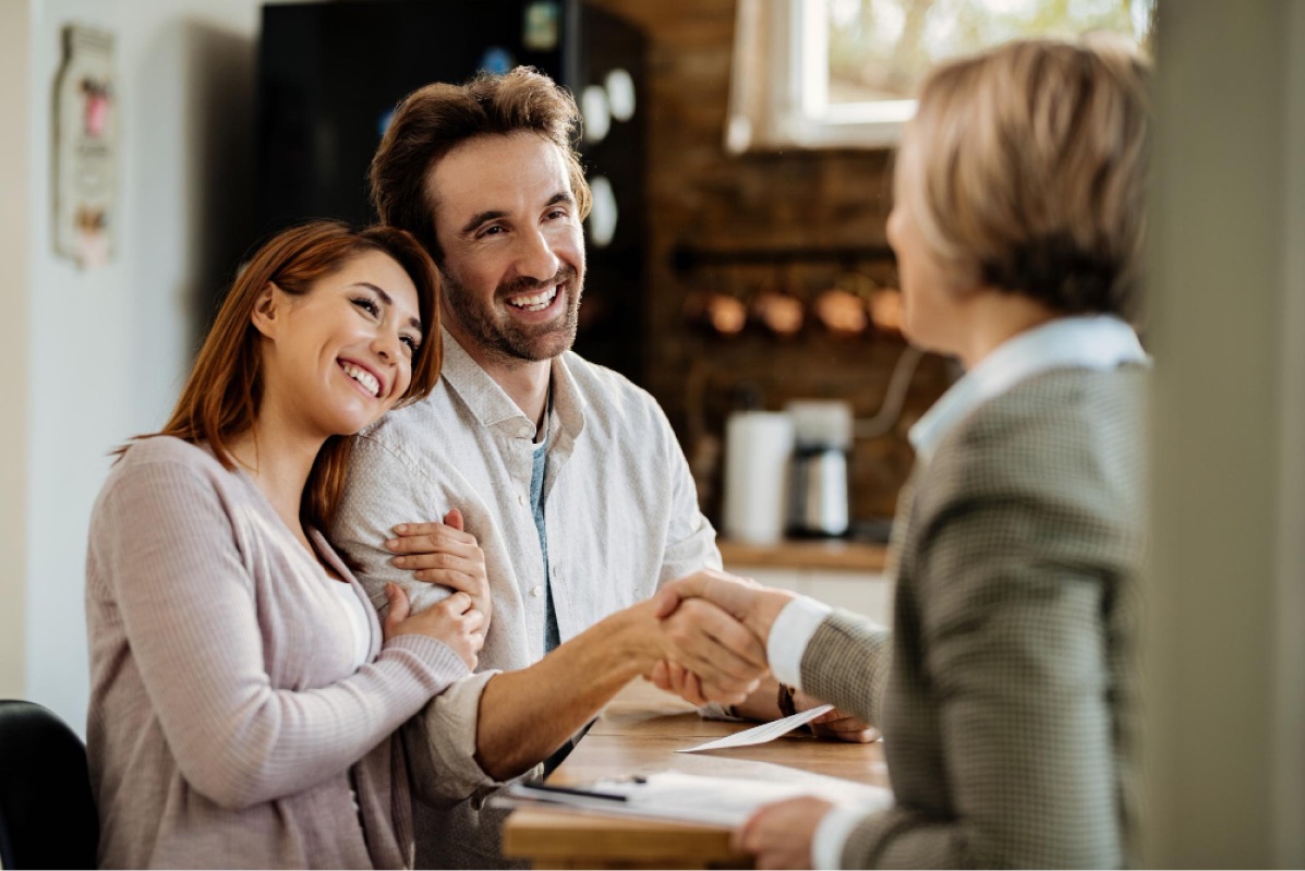 A realtor shaking hands with a couple after closing on their home